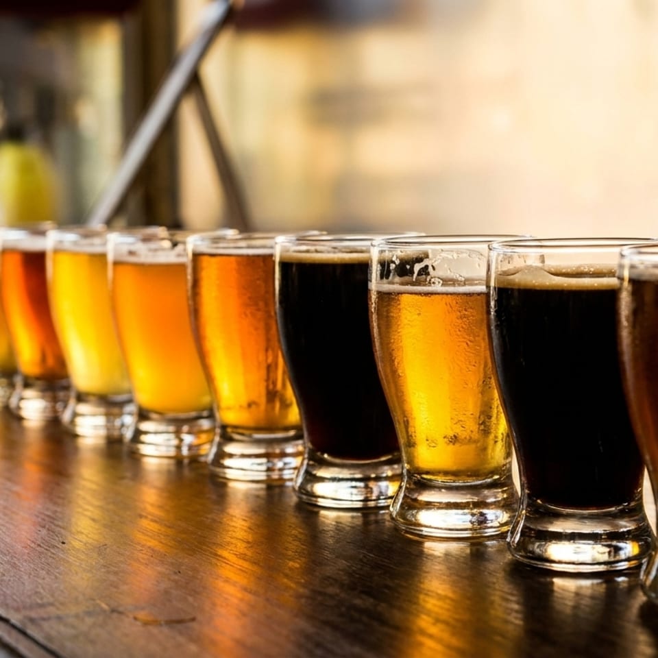 A row of beer tasting glasses on a wooden bar, showcasing various shades of lagers and stouts.