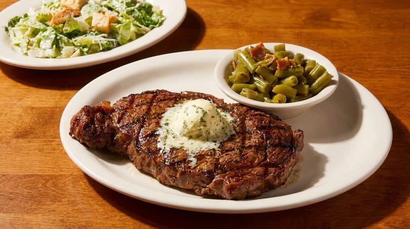 Grilled steak with melting butter, a side of green beans, and a Caesar salad.