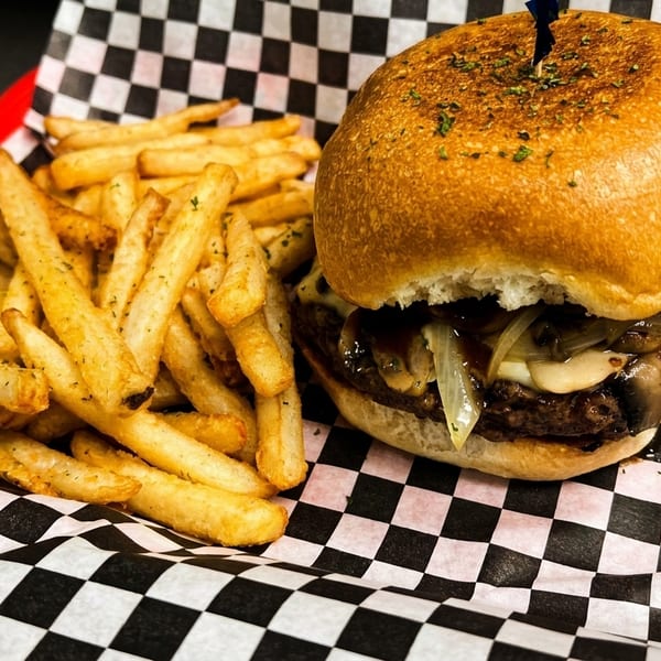 A juicy burger with mushrooms and onions, served with a side of golden fries in a red basket.