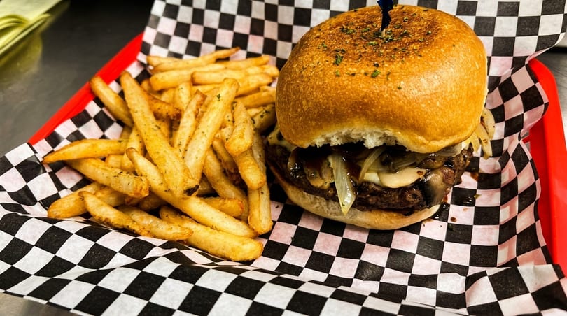 Gourmet burger with mushrooms and onions, served with a side of golden french fries.