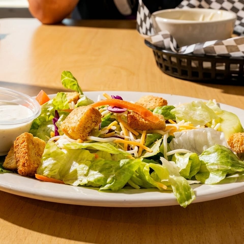 A fresh side salad with lettuce, cheese, croutons, and a side of ranch dressing on a wooden table.